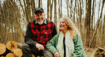 Paul and Lorraine Matthews resting on a log pile in a wooded area