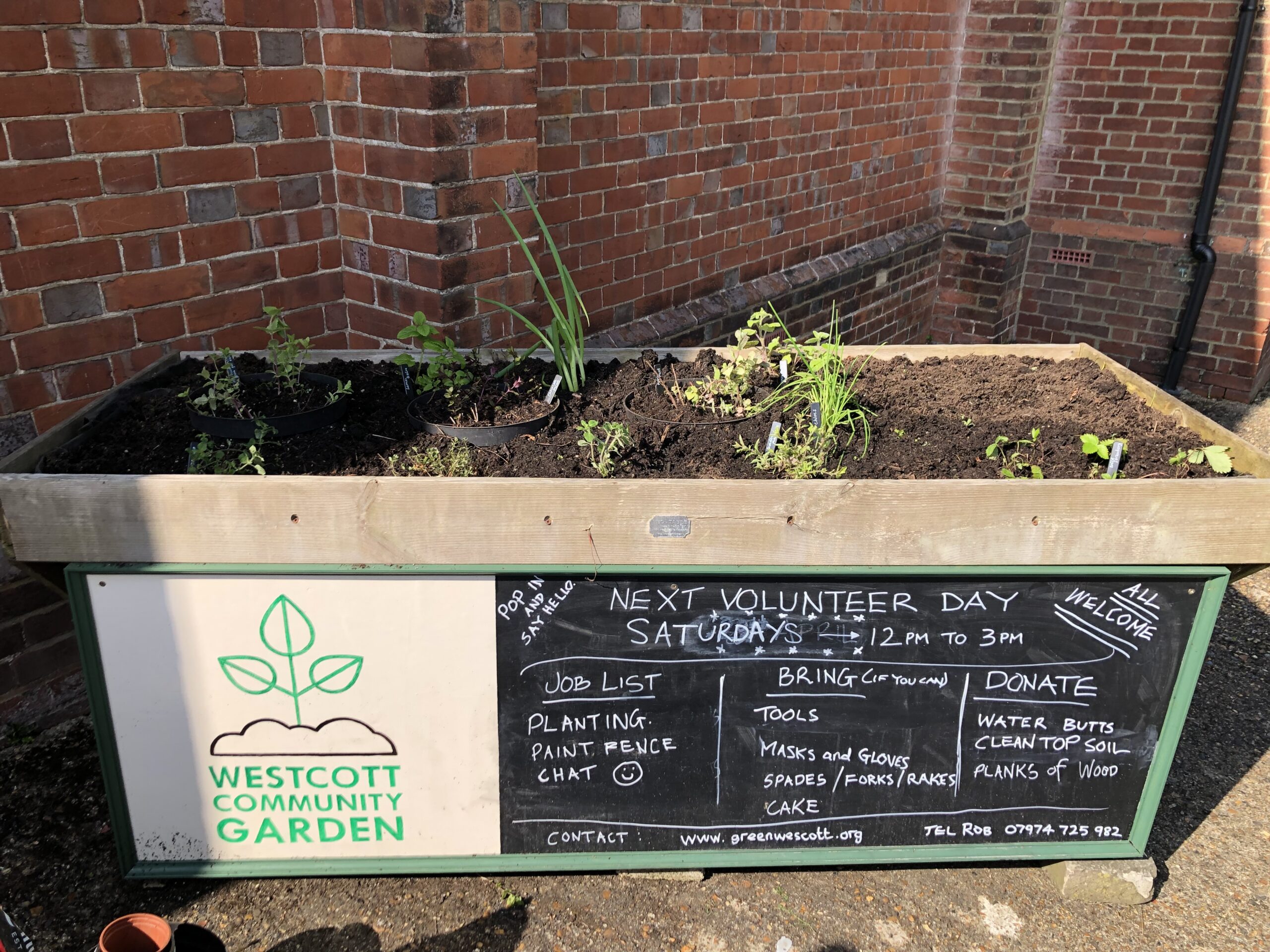Image of planter at Green Westcott Community Garden with a blackboard on the front showing information for volunteers